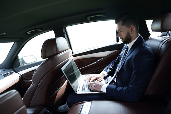 business man in the back of a car typing on a laptop