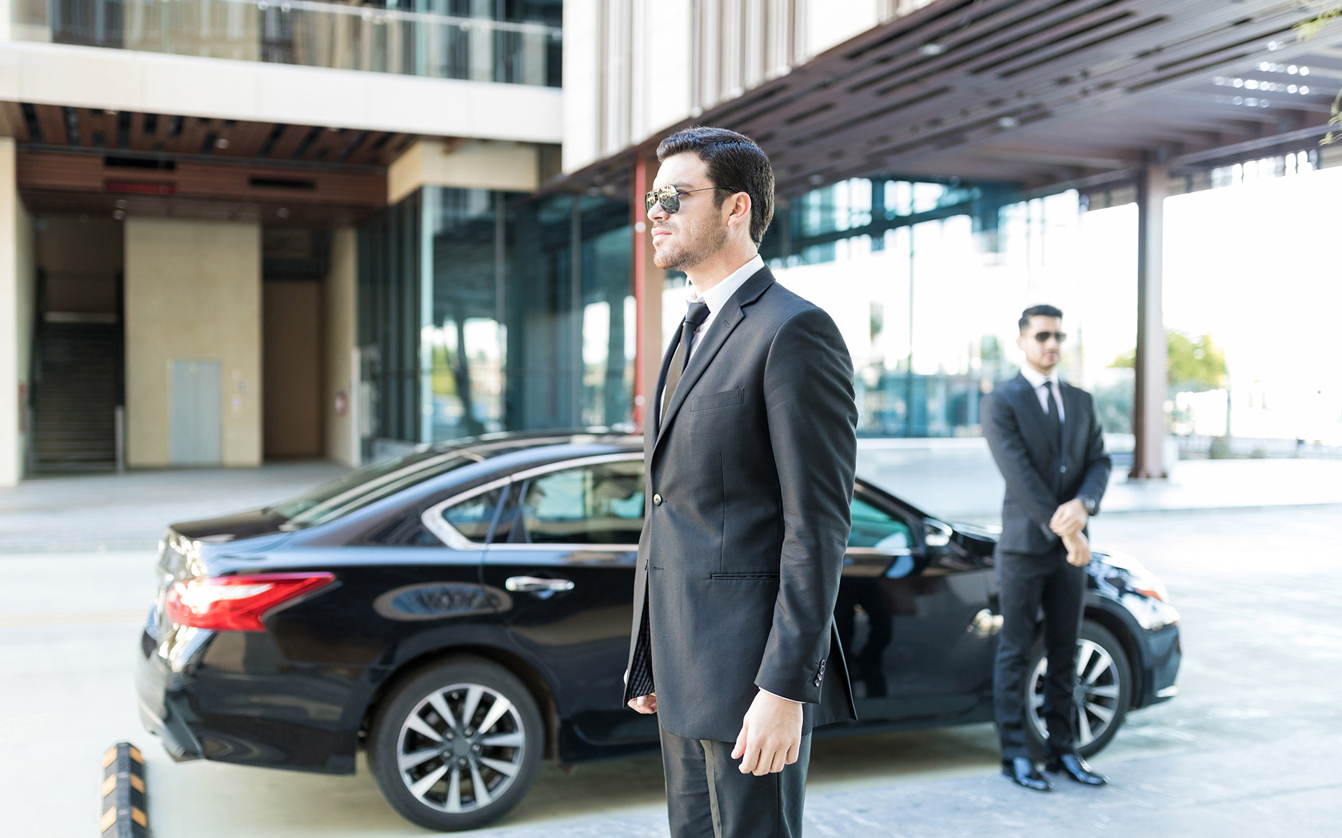 security in suits and sunglasses standing near a black car